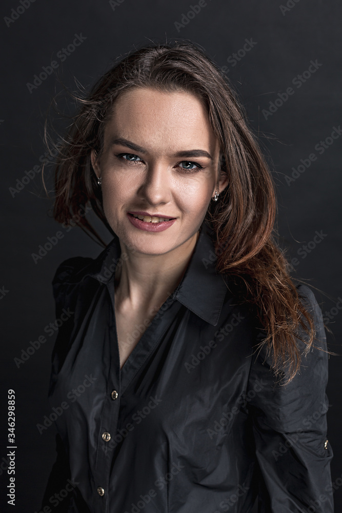 A makeup brunette girl in a black dress is standing and looking at the viewer. Studio portrait on a dark background. Vertical orientation. A makeup brunette girl in a black dress is standing and looking at the viewer. Studio portrait on a dark background. Vertical orientation.