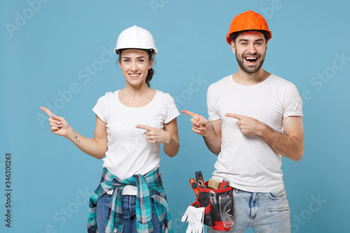 Smiling couple woman man in casual clothes protective helmet hardhat isolated on blue background. Instruments accessories for renovation apartment room. Repair home concept. Point index fingers aside. photo