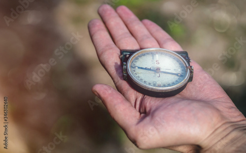Male holding a military compass in outstretched hand. Man holding an old compass on the palm of the hand showing direction. Outdoor photo, close up, blurred background. 