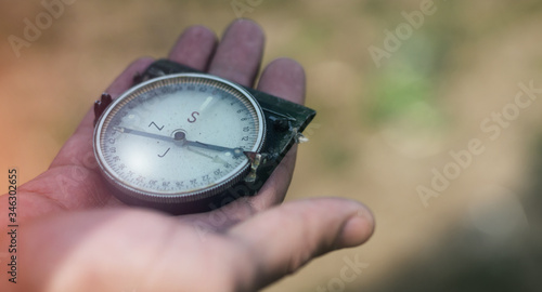 Man holding an old compass showing direction. Male holding a military compass with one outstretched hand. Outdoor photo, close up, blurred background, copy space.
