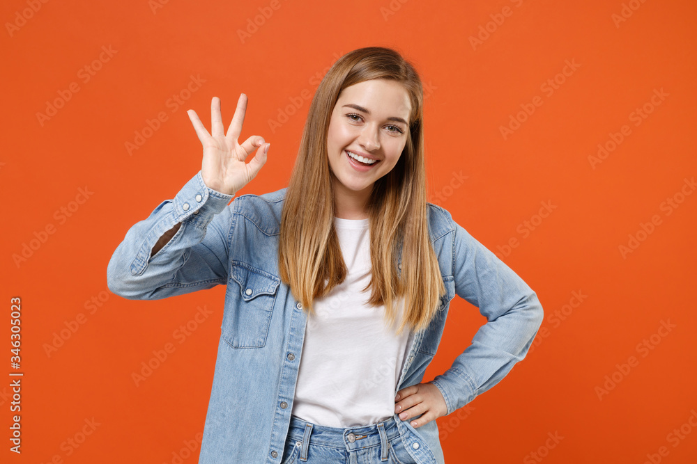 Funny young woman girl in casual denim clothes posing isolated on bright orange wall background studio portrait. People sincere emotions lifestyle concept. Mock up copy space. Showing OK gesture. Funny young woman girl in casual denim clothes posing isolated on bright orange wall background studio portrait. People sincere emotions lifestyle concept. Mock up copy space. Showing OK gesture.