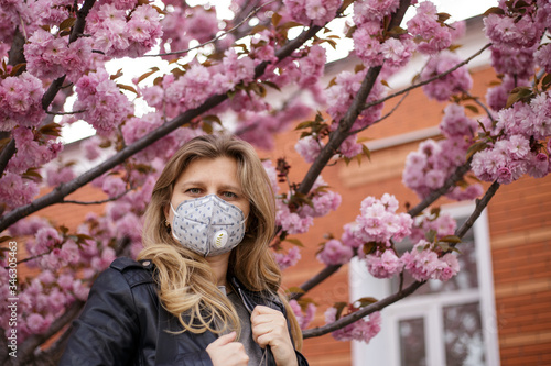 Girl in a mask a respirator. Quarantine isolation during a coronavirus pandemic. Portrait against the background of a blossoming sakura tree