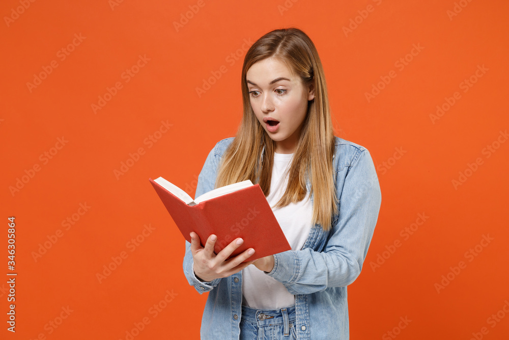 Shocked amazed young woman girl in casual denim clothes posing isolated on bright orange wall background studio portrait. People sincere emotions lifestyle concept. Mock up copy space. Reading book. Shocked amazed young woman girl in casual denim clothes posing isolated on bright orange wall background studio portrait. People sincere emotions lifestyle concept. Mock up copy space. Reading book.
