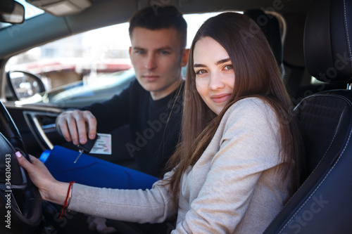 Happy girl in a new car receives a drivers license and keys from a young man. © Kobrinphoto