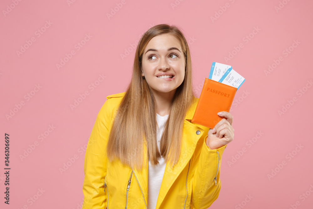Pensive young woman girl in yellow leather jacket posing isolated on pastel pink background. People lifestyle concept. Mock up copy space. Hold passport tickets boarding pass, biting lips, looking up. Pensive young woman girl in yellow leather jacket posing isolated on pastel pink background. People lifestyle concept. Mock up copy space. Hold passport tickets boarding pass, biting lips, looking up.