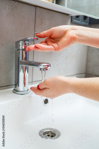 White sink with a silver faucet in the bathroom. Gray can with liquid soap for hands. Turning on the tap water, personal hand hygiene. Hand washing under running water