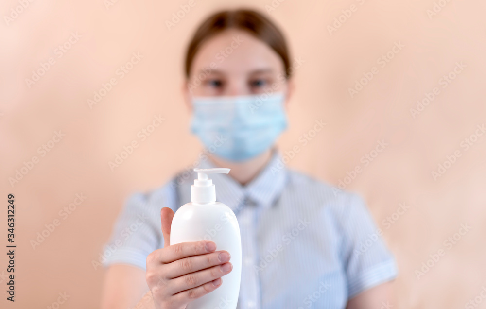 teenage girl in a protective medical mask covers her face, holds in her hand an antiseptic, liquid soap, for washing hands. Flu infection is a disease and pandemic. Beige background. teenage girl in a protective medical mask covers her face, holds in her hand an antiseptic, liquid soap, for washing hands. Flu infection is a disease and pandemic. Beige background.