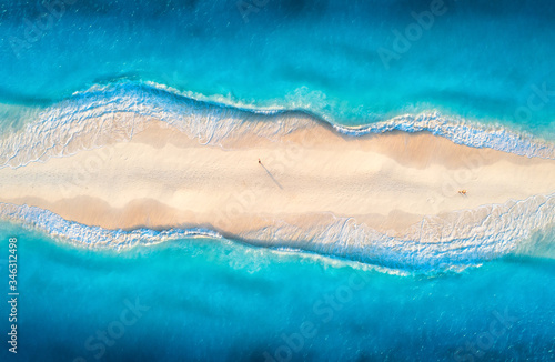 Aerial view of transparent blue sea with waves on the both sides and people on sandy beach at sunset. Summer travel in Zanzibar, Africa. Tropical landscape with lagoon, white sand and ocean. Top view