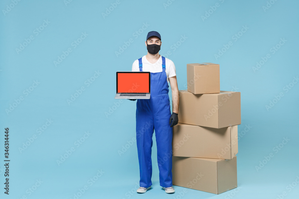 Full length delivery man in cap t-shirt uniform sterile face mask gloves isolated on blue background studio Guy employee courier hold box Service pandemic coronavirus virus covid-19 2019-ncov concept. Full length delivery man in cap t-shirt uniform sterile face mask gloves isolated on blue background studio Guy employee courier hold box Service pandemic coronavirus virus covid-19 2019-ncov concept.