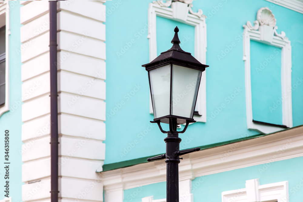 Iron black retro lantern with a glass shade on a pillar against the background of the facade of the building, closeup. Iron black retro lantern with a glass shade on a pillar against the background of the facade of the building, closeup.