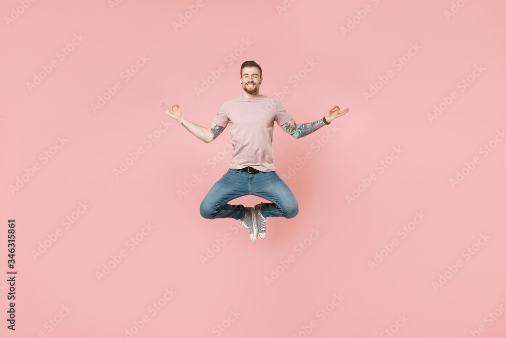 Smiling young tattooed man guy in pastel casual t-shirt posing isolated on pink background studio. People lifestyle concept. Mock up copy space. Jumping hold hands in yoga gesture relaxing meditating.
