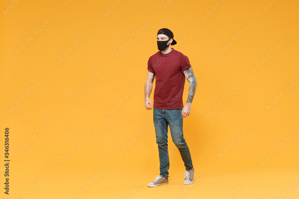 Fototapeta premium Young tattooed man guy in casual t-shirt cap black face mask posing isolated on yellow wall background studio portrait. People sincere emotions lifestyle concept. Mock up copy space. Looking aside.