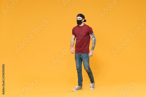 Young tattooed man guy in casual t-shirt cap black face mask posing isolated on yellow wall background studio portrait. People sincere emotions lifestyle concept. Mock up copy space. Looking aside.