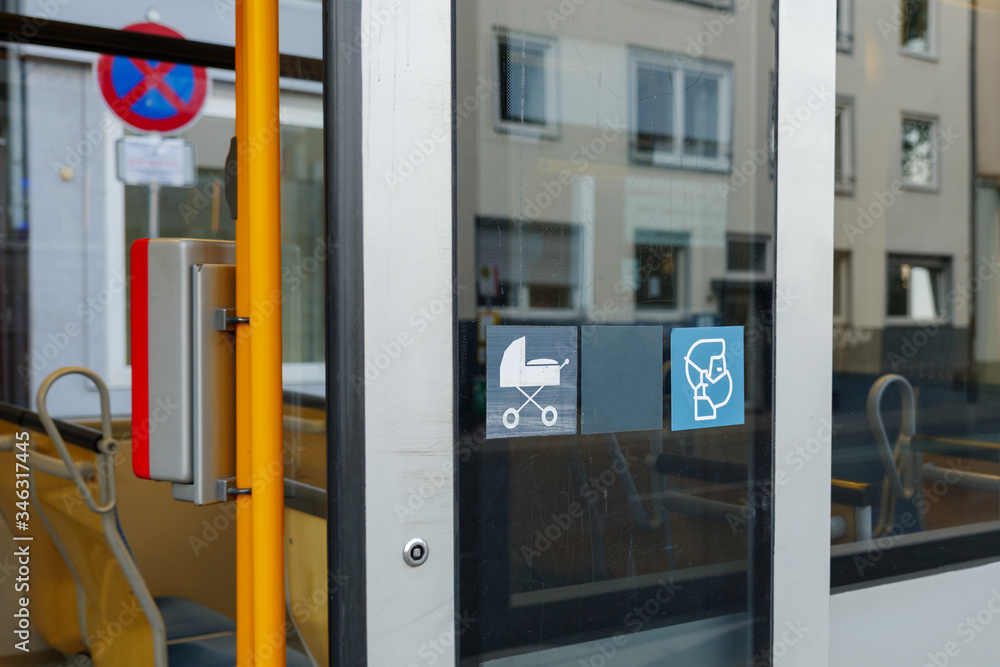 Selected focus at face mask covering mouth and nose symbol on blue sign on glass of public transportation's window door in Germany during epidemic of COVID-19 virus and German face mask regulations.