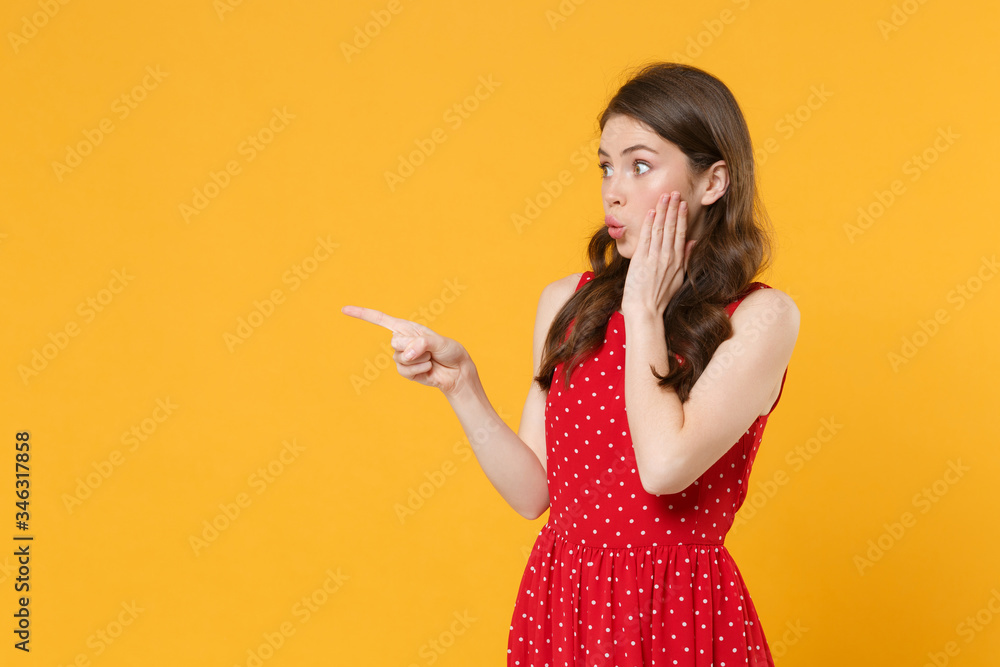 Shocked young brunette woman girl in red summer dress posing isolated on yellow background studio portrait. People lifestyle concept. Mock up copy space. Pointing index finger aside put hand on cheek. Shocked young brunette woman girl in red summer dress posing isolated on yellow background studio portrait. People lifestyle concept. Mock up copy space. Pointing index finger aside put hand on cheek.
