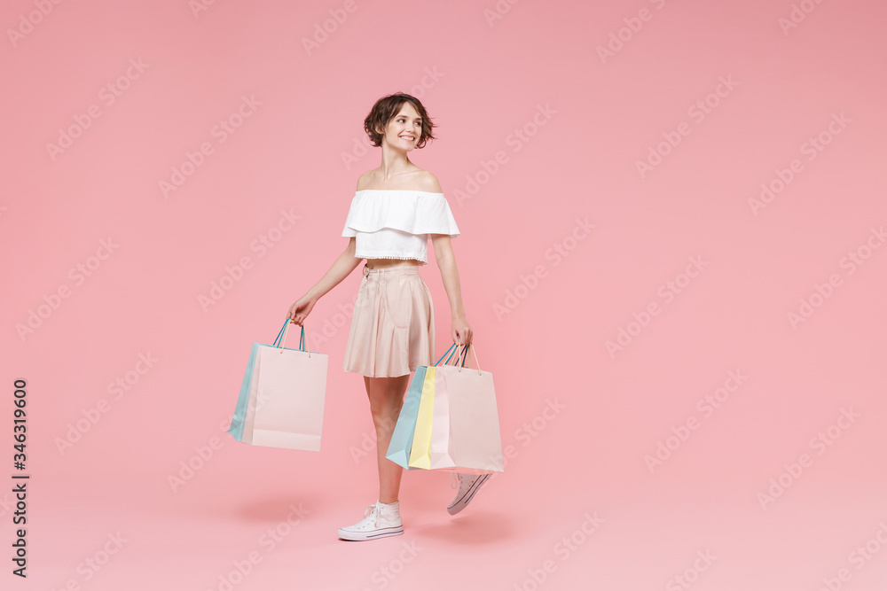 Smiling young woman girl in summer clothes hold package bag with purchases isolated on pastel pink wall background studio portrait. Shopping discount sale concept. Mock up copy space. Looking aside.
