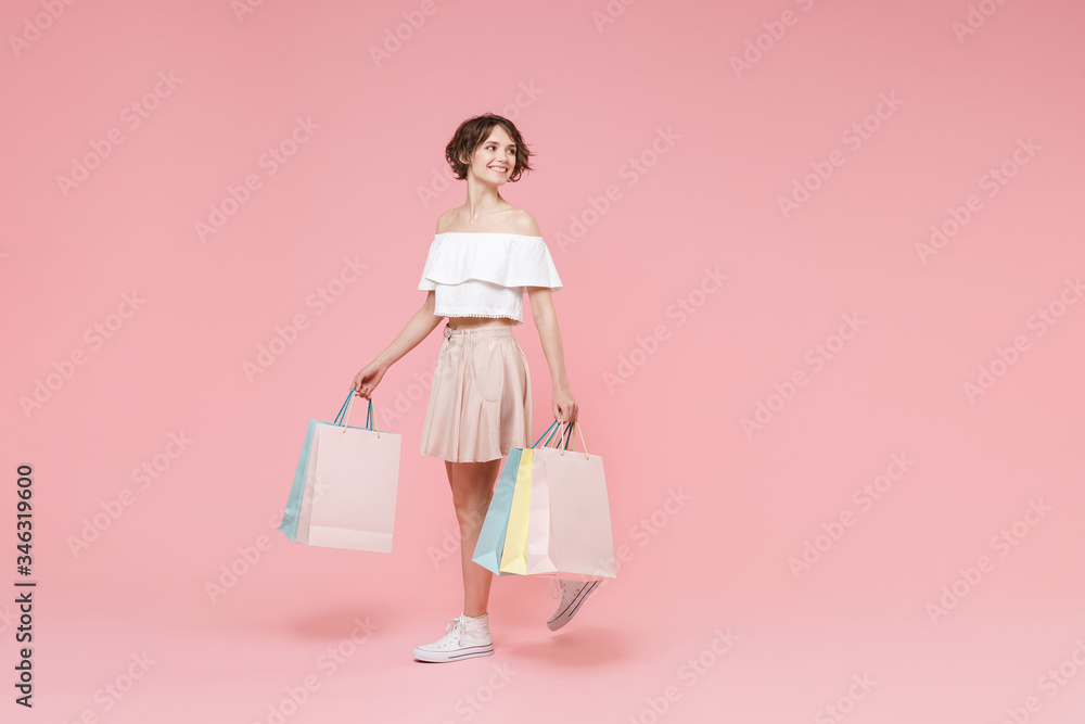 Smiling young woman girl in summer clothes hold package bag with purchases isolated on pastel pink wall background studio portrait. Shopping discount sale concept. Mock up copy space. Looking aside. Smiling young woman girl in summer clothes hold package bag with purchases isolated on pastel pink wall background studio portrait. Shopping discount sale concept. Mock up copy space. Looking aside.