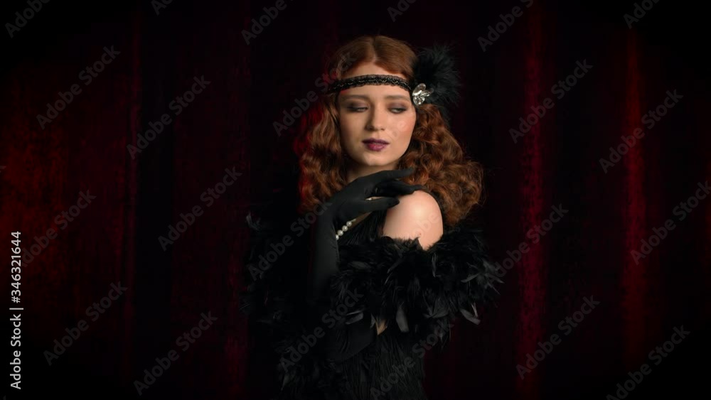 Old-fashioned sexy woman dressed in style of Flappers posing on dark background. Roaring twenties, retro, party, fashion concept Old-fashioned sexy woman dressed in style of Flappers posing on dark background. Roaring twenties, retro, party, fashion concept