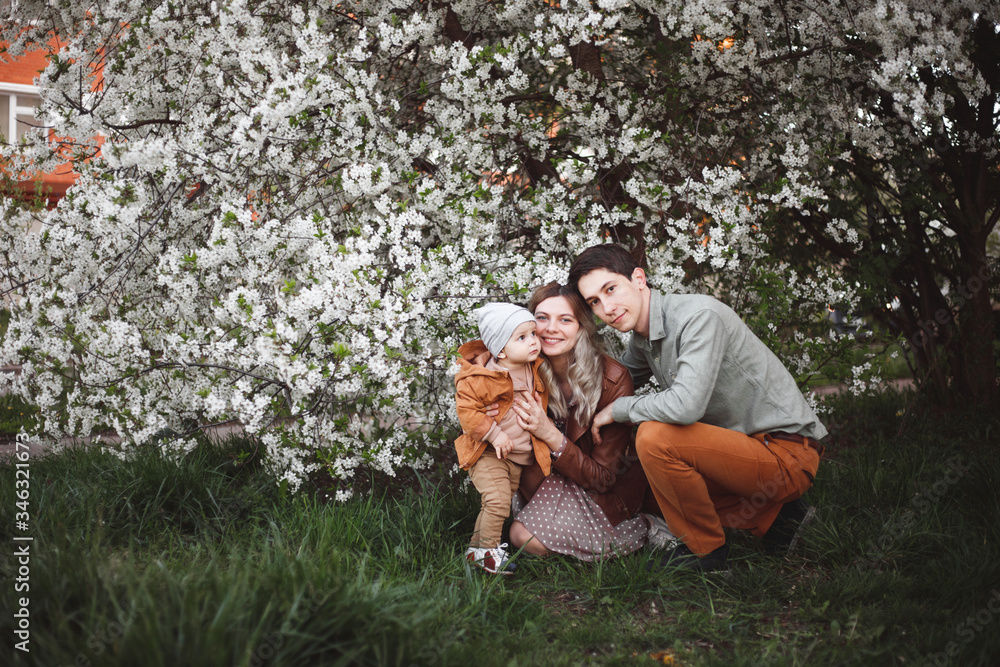 Fototapeta premium Beautiful young parents and their cute little son have fun near flowering trees