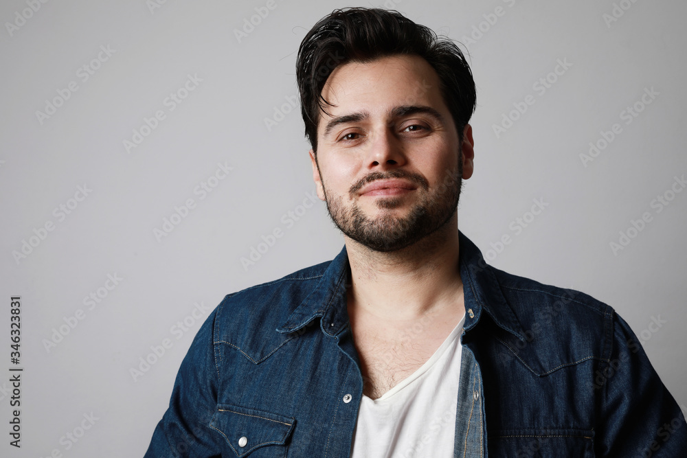 Bearded man in the denim outfit which mixed with bright white t-shirt posing over white wall. Space for text. Bearded man in the denim outfit which mixed with bright white t-shirt posing over white wall. Space for text.