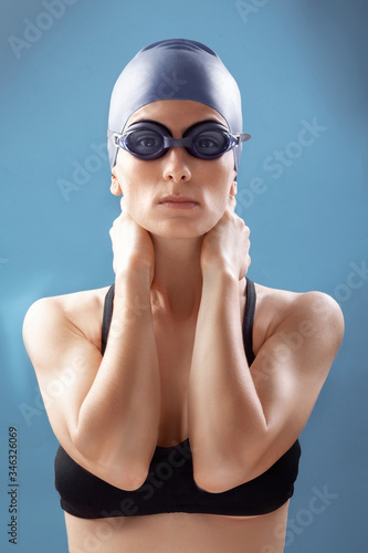 Portrait of female swimmer with cap and goggles on grey background