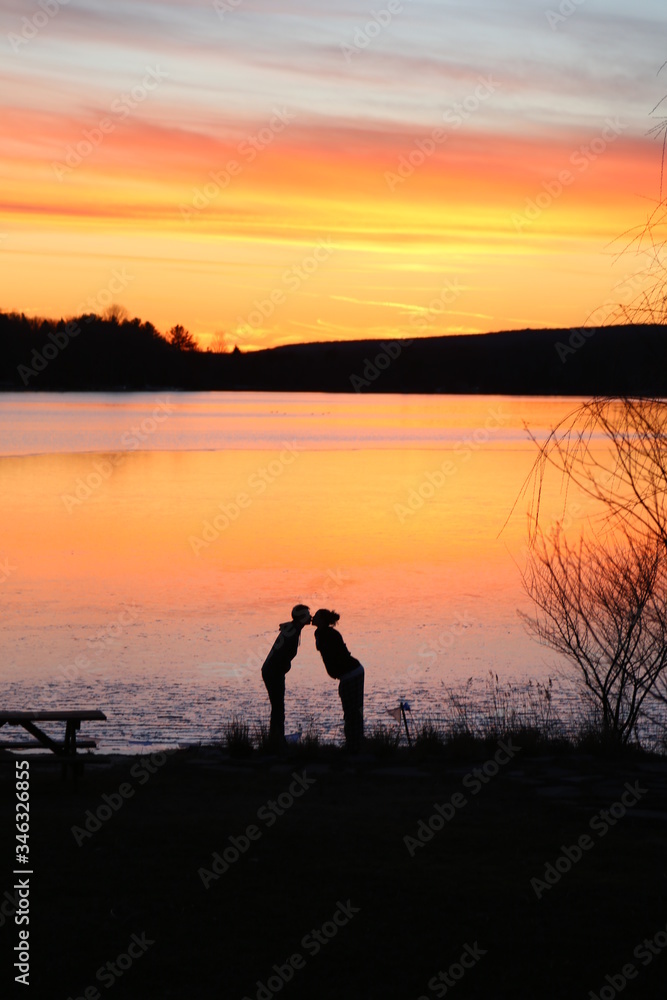 silhouette of man and woman kissing on the beach at sunset beside a lake