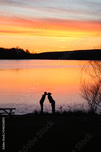 silhouette of man and woman kissing on the beach at sunset beside a lake