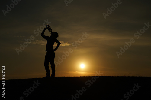 Fototapeta Naklejka Na Ścianę i Meble -  夕暮れの丘で水を飲む男性