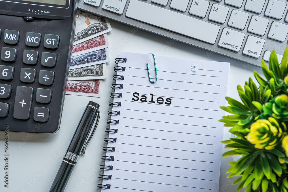 Sales text with notepad, paper clip, keyboard, decorative flower, fountain pen, calculator and banknotes currency on white background. Business and Copy space concept. Sales text with notepad, paper clip, keyboard, decorative flower, fountain pen, calculator and banknotes currency on white background. Business and Copy space concept.