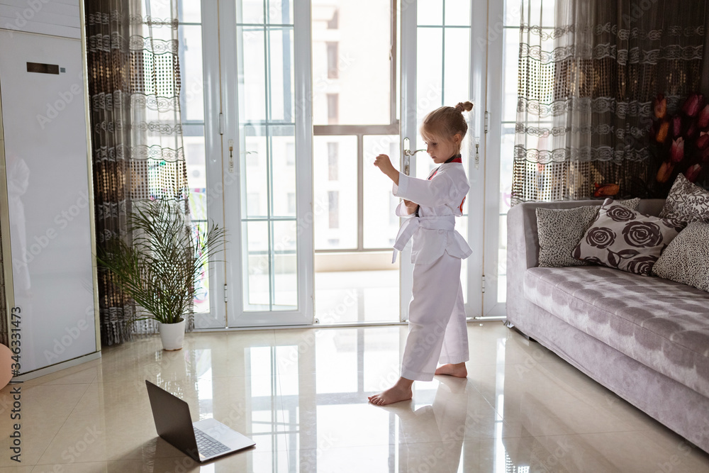 Taekwondo girl in kimono with white belt exercising at home in living room. Online education during coronavirus covid-19 lockdown, self isolation and social distancing concept. Taekwondo girl in kimono with white belt exercising at home in living room. Online education during coronavirus covid-19 lockdown, self isolation and social distancing concept.