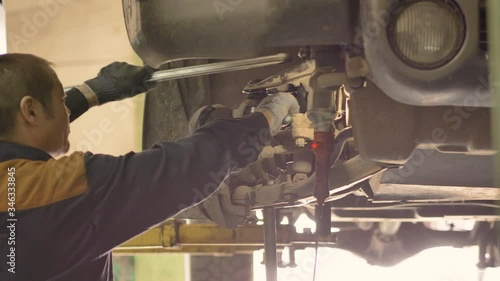 An Asian man is repairing the chassis of an old car lifted on a lift in a workshop, close-up.