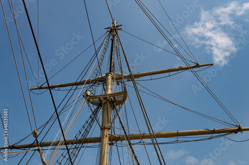 Detail view of an old tall ship mast and rigging, old wooden sailing vessel with rigging lines against a beautiful blue sky, horizontal aspect