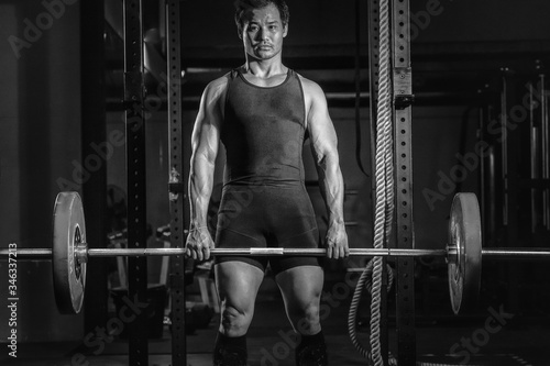 asian athletic strong man having workout and bodybuilding with weight lifting deadlift style in gym and fitness club in dark tone