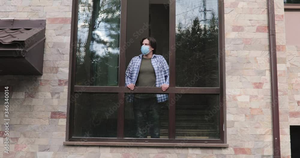 Man in mask comes to opened window, leans on it, looks around and breathes air