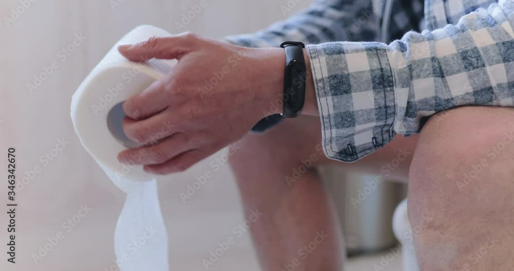 Man uncoiling toilet paper roll when suffering diarrhea on the lavatory pan Man uncoiling toilet paper roll when suffering diarrhea on the lavatory pan