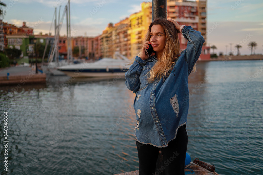 Young pregnant girl in harbor with lot of yachts 