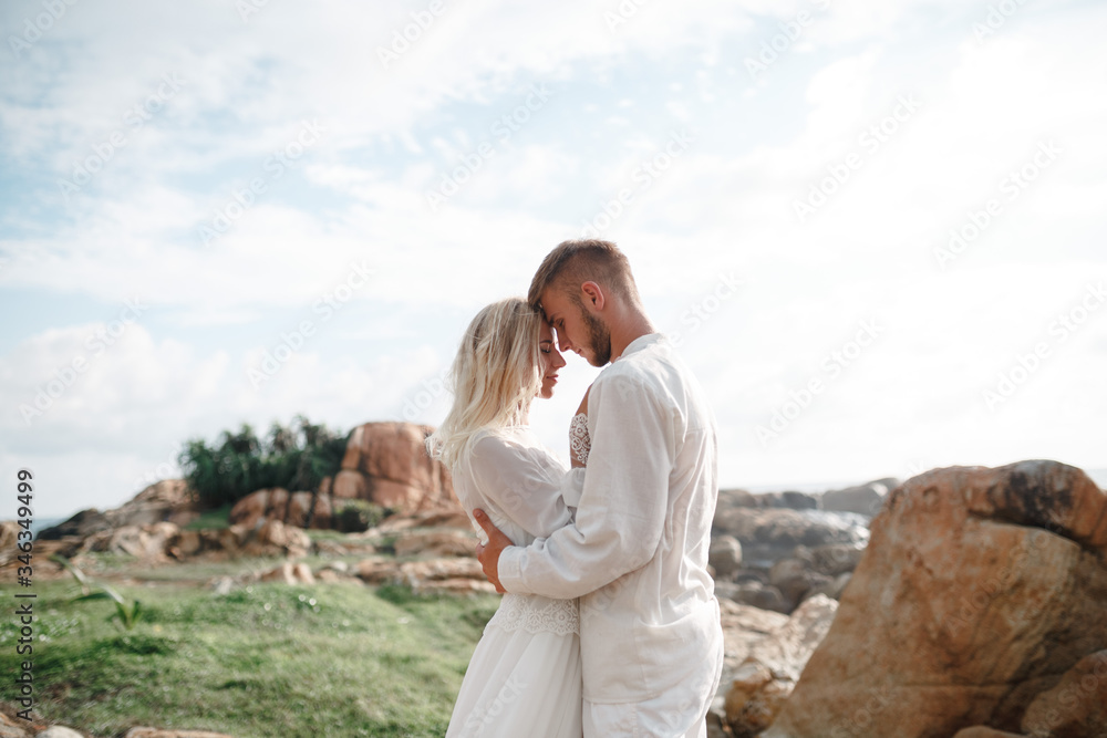 Beautifull wedding couple kissing and embracing near the shore of indian ocean standing on sea cliff. Close up happy young wedding couple with sea on the mountain