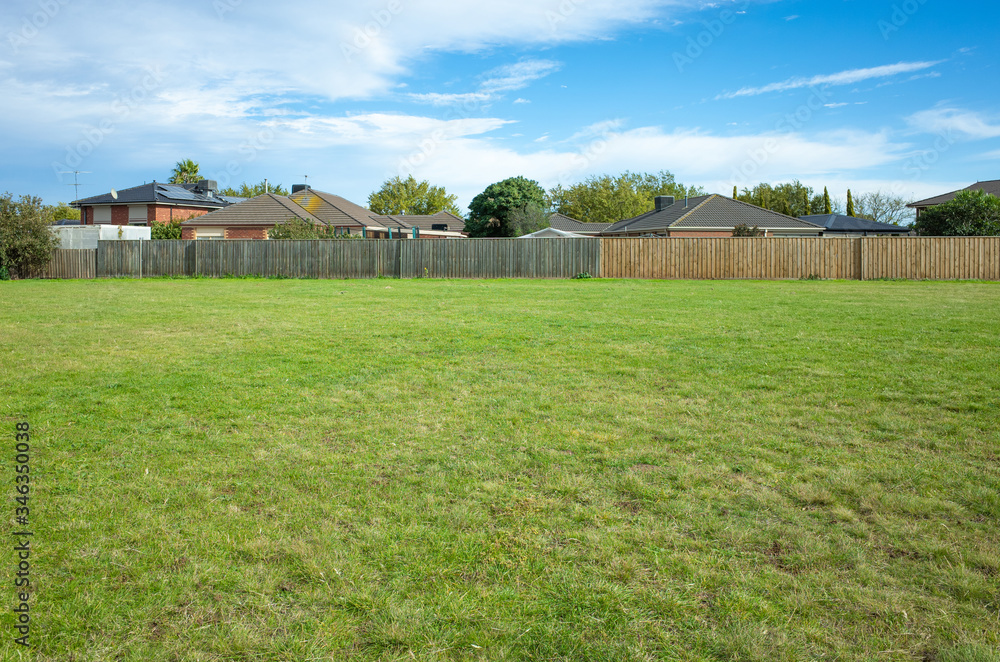Obraz premium Background texture of a large public local park with green and healthy grass and with some trees and residential houses in the distance. Melbourne, VIC Australia