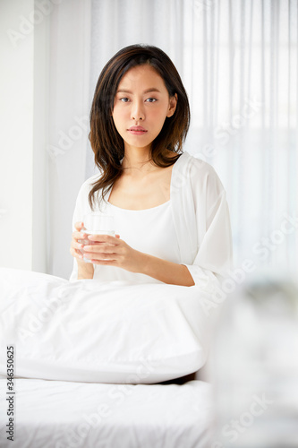 Happy girl and white sleepwear wake up in the morning sitting in front of light window and hold water drinking. Morning concept