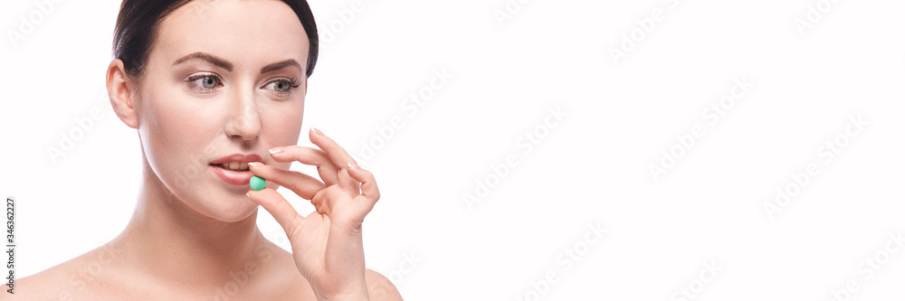 Girl holding a pill. Vitamins concept. Beautiful portrait on white background. Medicine home routine. Female morning supplement. Meds anti allergy drug. Horizontal banner Girl holding a pill. Vitamins concept. Beautiful portrait on white background. Medicine home routine. Female morning supplement. Meds anti allergy drug. Horizontal banner