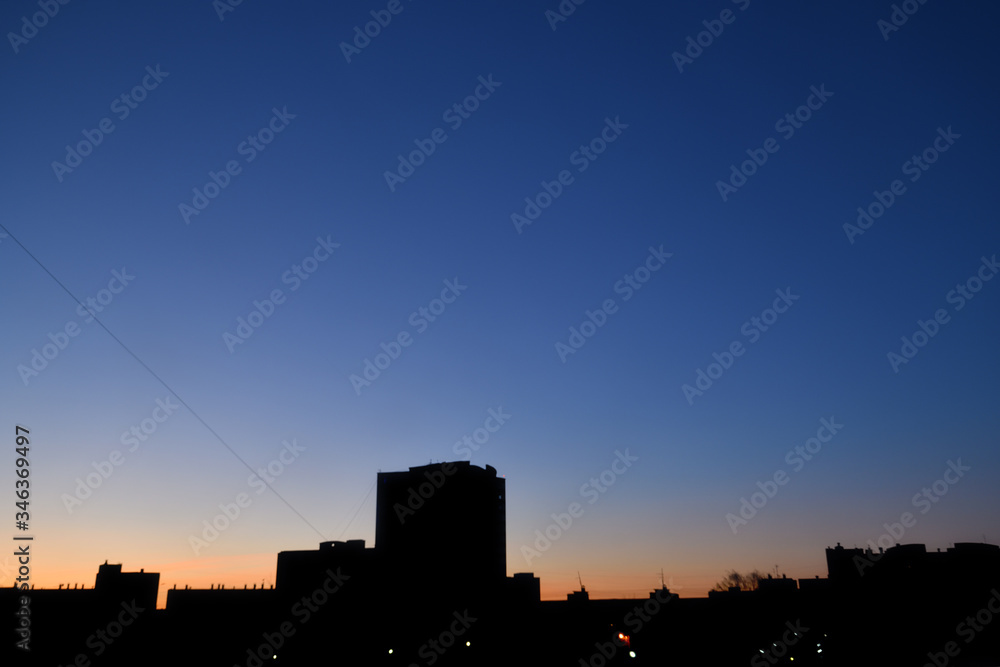 Dawn. Urban landscape at dawn: beautiful sunset in the city with orange  sky and black silhouettes of high residential apartment buildings, view through the window Horizontal photo