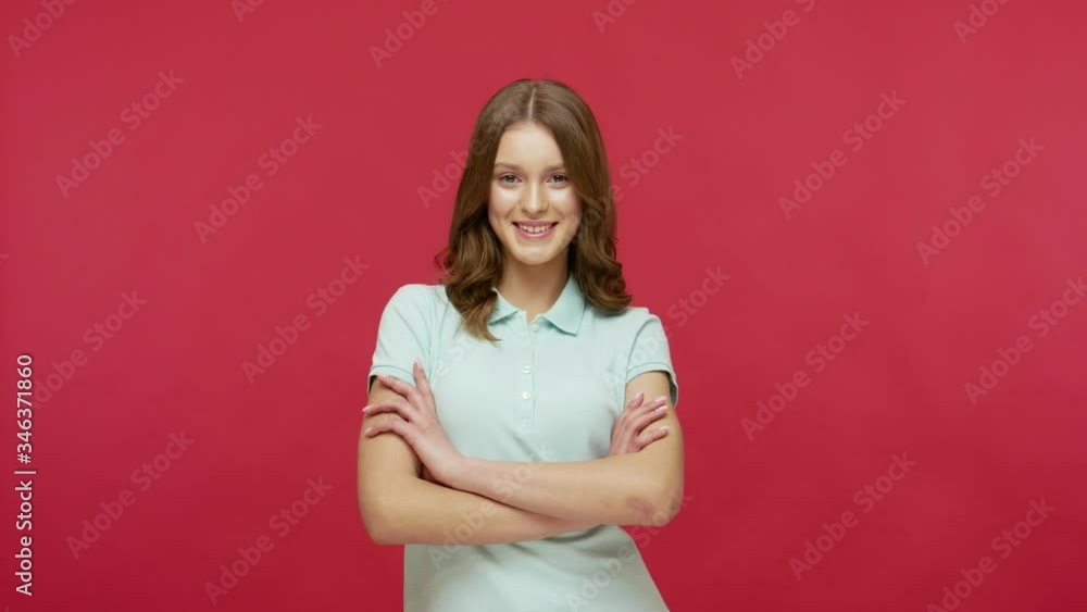Happy young brunette woman in polo t-shirt turning to camera with crossed hands and looking with satisfied optimistic expression, positive emotions. indoor studio shot isolated on red background Happy young brunette woman in polo t-shirt turning to camera with crossed hands and looking with satisfied optimistic expression, positive emotions. indoor studio shot isolated on red background