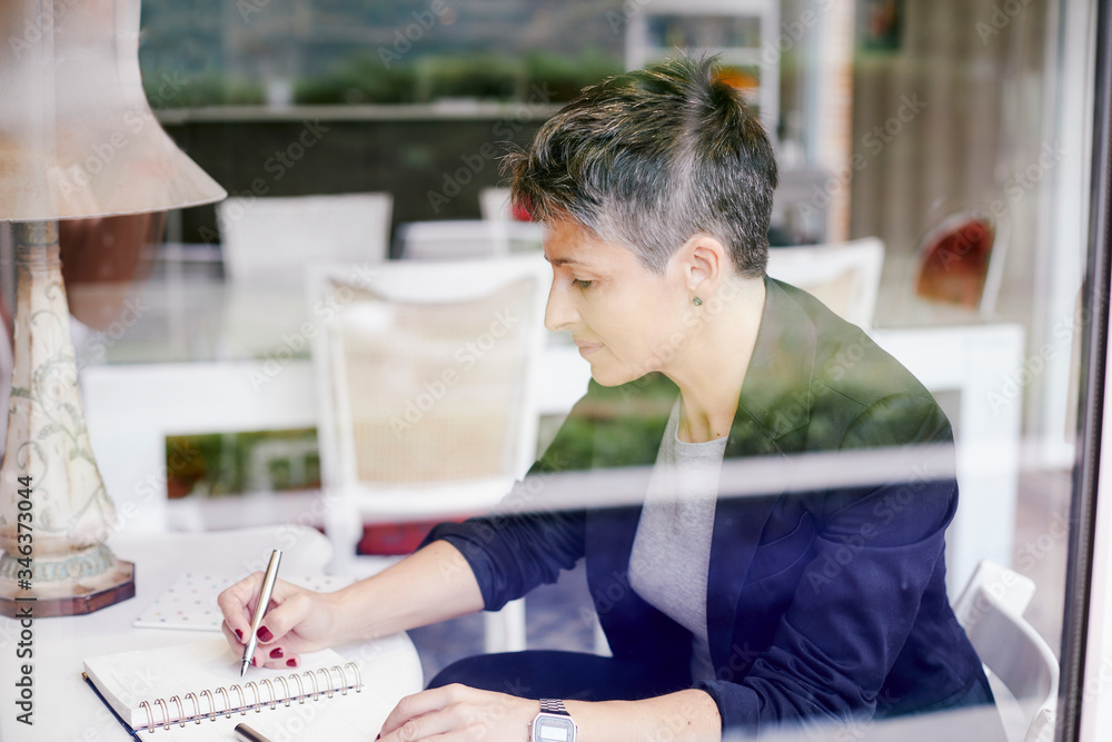 Businesswoman writing with concentration seen through a glass Businesswoman writing with concentration seen through a glass