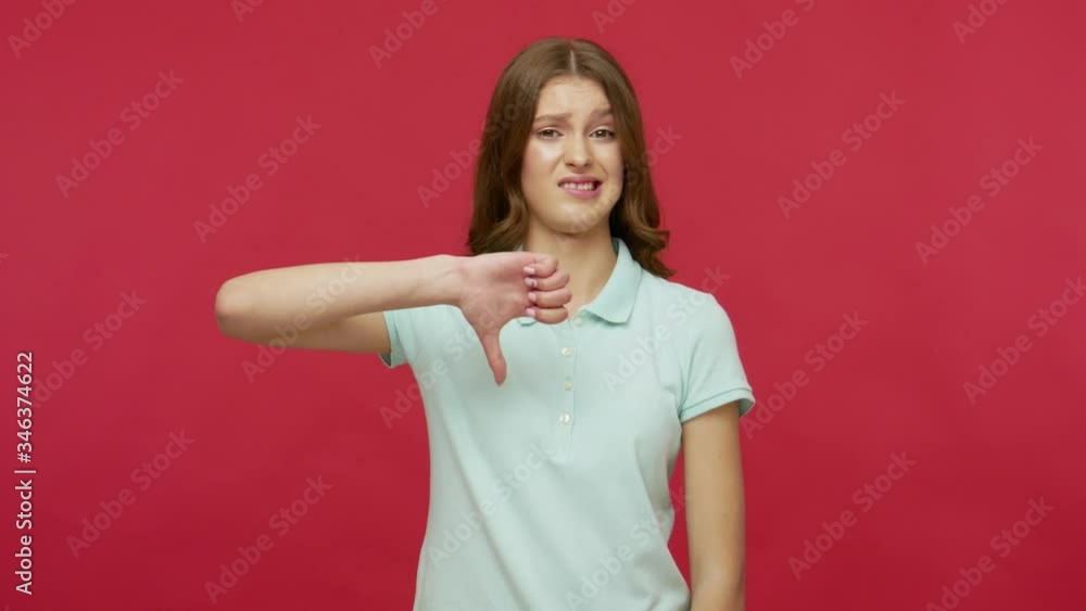 Dislike, bad choice! Dissatisfied cranky young brunette woman in polo t-shirt showing thumbs down, expressing disapproval and critique to failed project. indoor studio shot isolated on red background Dislike, bad choice! Dissatisfied cranky young brunette woman in polo t-shirt showing thumbs down, expressing disapproval and critique to failed project. indoor studio shot isolated on red background