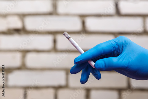 A hand in a blue rubber glove holds a cigarette
