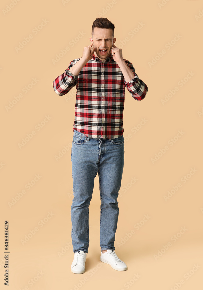 Young man suffering from loud noise on color background Young man suffering from loud noise on color background