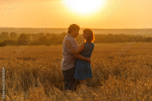 An adult farmer and his wife are hugging in their wheat field.