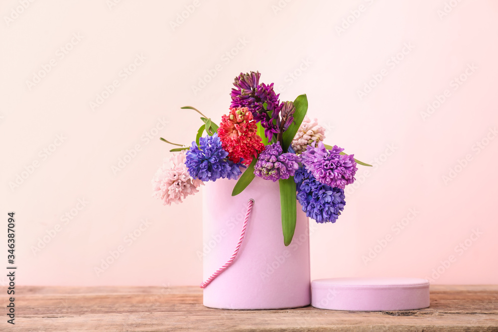 Box with beautiful hyacinth flowers on table against color background