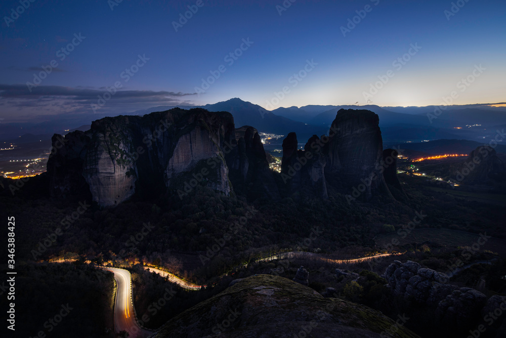 Fototapeta premium Meteora rocks at evening night time with light from city