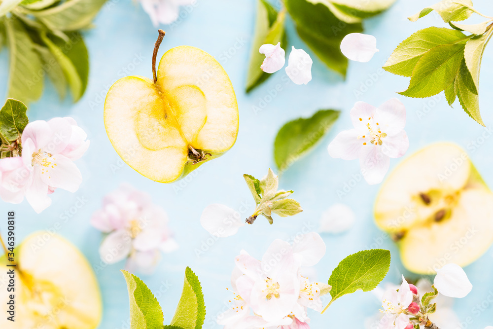 Obraz premium Apples, flowers and leaves of an apple tree in flight. Fresh spring texture leaves of different sizes on a blue background. The concept of spring flowering or packaging of juice.